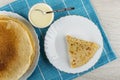 Stack of russian pancakes in white dish, spoon in bowl with condensed milk, pancake in plate on blue napkin on wooden table. Top