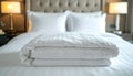 Folded white comforter on a neatly made hotel bed with tufted headboard and bedside lamps Royalty Free Stock Photo
