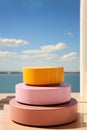 A stack of three pink and yellow product display podiums for natural product. Circular shape base. Sea on background