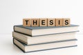 A stack of three textbooks displayed with wood blocks spelling THESIS presented on white table Royalty Free Stock Photo