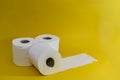A stack of three white disposable toilet rolls on a yellow background. One roll lies untwisted. Soft fresh cotton. Essential goods