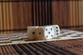 Stack of three white plastic dices on brown wooden board background. Six sides cube with black dots. Random number