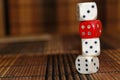 Stack of three white plastic dices and one red dice on brown wooden board background. Six sides cube with black dots. Number 3, 4,