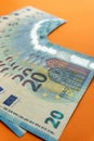 A stack of used blue 20 euro banknotes on a vivid orange background.