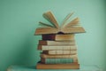 Stack of vintage books with open book on top, suggesting knowledge, learning, and literature, against a teal background Royalty Free Stock Photo