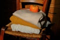 Stack of warm knitted sweaters in sunlight on wooden chairs across wooden dresser close-up and orange persimmon on the top. Warm c Royalty Free Stock Photo