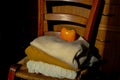 Stack of warm knitted sweaters in sunlight on wooden chairs across wooden dresser close-up and orange persimmon on the top. Warm c Royalty Free Stock Photo