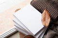 Stack of white blank books with autumn leaves and cup of hot tea on old wooden chair, mockup design