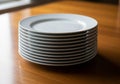 A stack of white ceramic dinner plates is placed neatly on a wooden table. The plates are identical Royalty Free Stock Photo