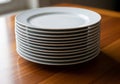 A stack of white ceramic plates is neatly arranged on a wooden table. The plates are round with a Royalty Free Stock Photo