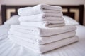 Stack of white clean bath towels on bed sheet in modern hotel bedroom interior, copy space.