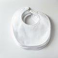 A stack of white cotton baby bibs lays on a light surface. Each bib features a rounded Royalty Free Stock Photo