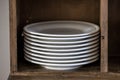 A stack of white porcelain dinner plates in a wood cabinet in a home or restaurant Royalty Free Stock Photo