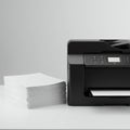 Stack of white printer paper next to a black multifunction printer featuring a control