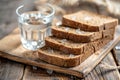 Stack of Whole Grain Bread with Seeds on Rustic Wooden Table beside a Clear Glass of Water Royalty Free Stock Photo