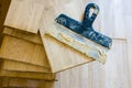 Stack of wood parquet or floorboard as floor covering with spatula on it with parquet adhesive glue on it top view. Preparation fo