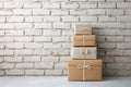 Stack of wrapped gift boxes in neutral tones with simple ribbons placed against a white brick wall, creating a Royalty Free Stock Photo