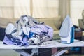 Stack of wrinkle clothes and electric iron on ironing board Royalty Free Stock Photo