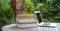 Stacked of books next to computer laptop. Garden view