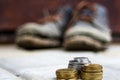 Stacked coins on blurred background of a pair of dirty old boots.