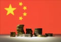 Stacked coins on a white table and a China flag in a background