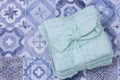 Stacked green face towels flannels tied with ribbon and a bow. On a blue tiled surface