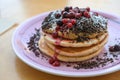 Stacked pancakes with peanut butter cream, berries, crumble and icing sugar on a plate, sweet breakfast, brunch or dessert dish,