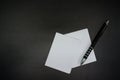 Stacked paper of blank white business cards simulated with an elegant black pen on a black background.