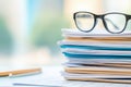 Stacked paperwork with eyeglasses resting on the top in a bright office environment during the day Royalty Free Stock Photo