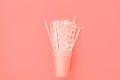 Stacked Pink Drinking Paper Cups with Striped Straws on Trendy Living Coral Color Background. Flat Lay Composition