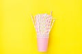 Stacked Pink Drinking Paper Cups With Striped Straws On Yellow Background. Flat Lay Composition. Birthday Party Celebration Kids
