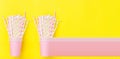 Stacked Pink Drinking Paper Cups with Striped Straws on Yellow Background. Flat Lay Composition. Birthday Party Celebration Kids
