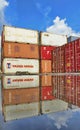 Stacked shipping containers reflect in puddle, blue sky and clouds