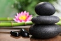 Stacked spa stones, bamboo stems and flower on wooden table against blurred background, closeup. Space for text Royalty Free Stock Photo