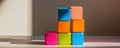 A stacked tower of brightly colored cubes, standing precariously on a light reflective surface