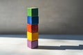 A stacked tower of multi-colored cubes on a light gray surface, with each cube casting a different