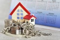 Stacking coins for house loan monthly installment with the metal cahin and lock pad infront of the red roof house and the desk cal