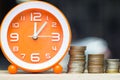 Stacking growing coins, Moneybags and orange clock on wooden tab Royalty Free Stock Photo