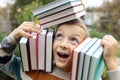 stacks of books on head shoulders of cheerful funny 8 year old boy. back to school