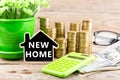 Stacks of coins and dollar bills, calculator, blackboard in the shape of a house with text & x22;NEW HOME& x22; Royalty Free Stock Photo