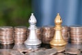 Stacks of dollar coins in front of two chess pieces of both sides in a duel Royalty Free Stock Photo