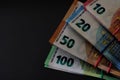 Stacks of 10, 20, 50 and 100 euro banknotes, tied with rubber band and fixed in the form of a fan, on a grey background.