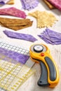 Stacks of multi-colored pieces of fabric, cutting mat, ruler, rotary cutter on a white surface