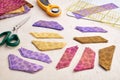 Stacks of multi-colored pieces of fabric, scissors, rotary cutter, cutting mat, ruler on a white surface