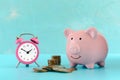 Stacks and a pile of coins, a pink alarm clock and a piggy bank on a turquoise background. The symbol of the Royalty Free Stock Photo