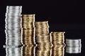 Stacks of silver and golden coins on surface with reflection isolated on black.