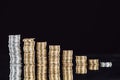 Stacks of silver and golden coins on surface with reflection isolated on black.