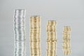 Stacks of silver and golden coins on surface with reflection isolated on grey.