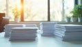 Stacks of white paper sit on sunny desk near window, suggesting office environment. Piles of documents symbolize work, Royalty Free Stock Photo