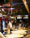 A staff of a Christmas market stands stirring the gigantic hot pan filled with pasta and cheese